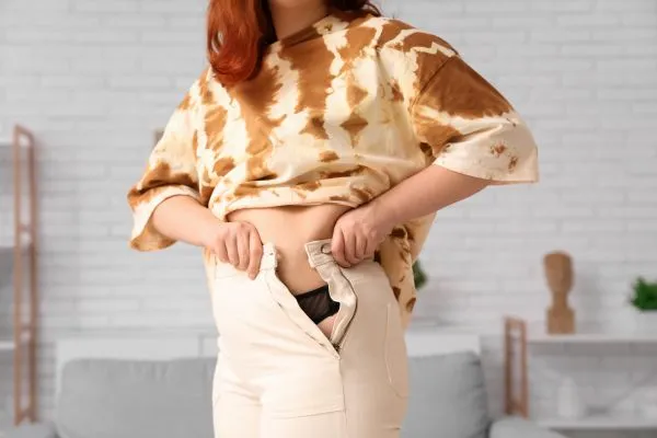 Image of woman trying to do her trousers up after pregnancy weight gain Hamilton